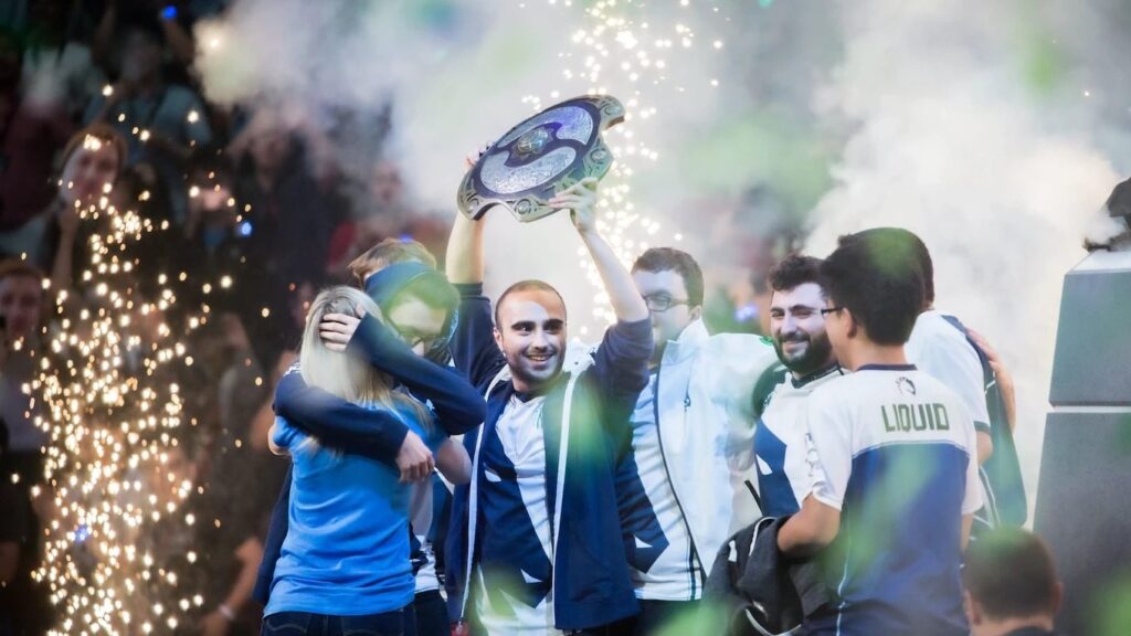 Team Liquid Dota 2 team holds up The International trophy amid confetti and stage lights.