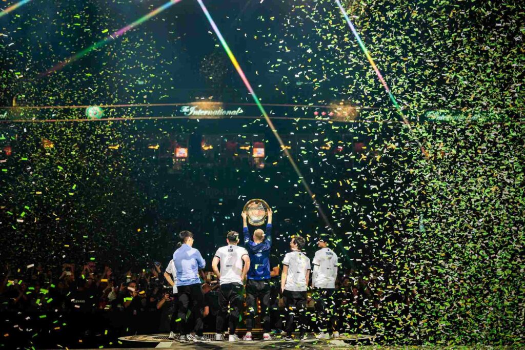 Team Liquid players celebrate a championship victory with confetti and the Aegis trophy on stage.