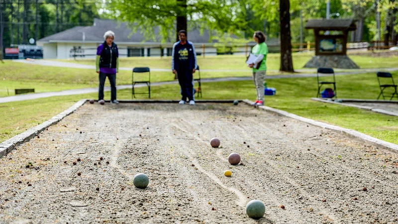 Photo showing a few people playing bocce (one of the world's most accessible sports) with bocce stones in the foreground