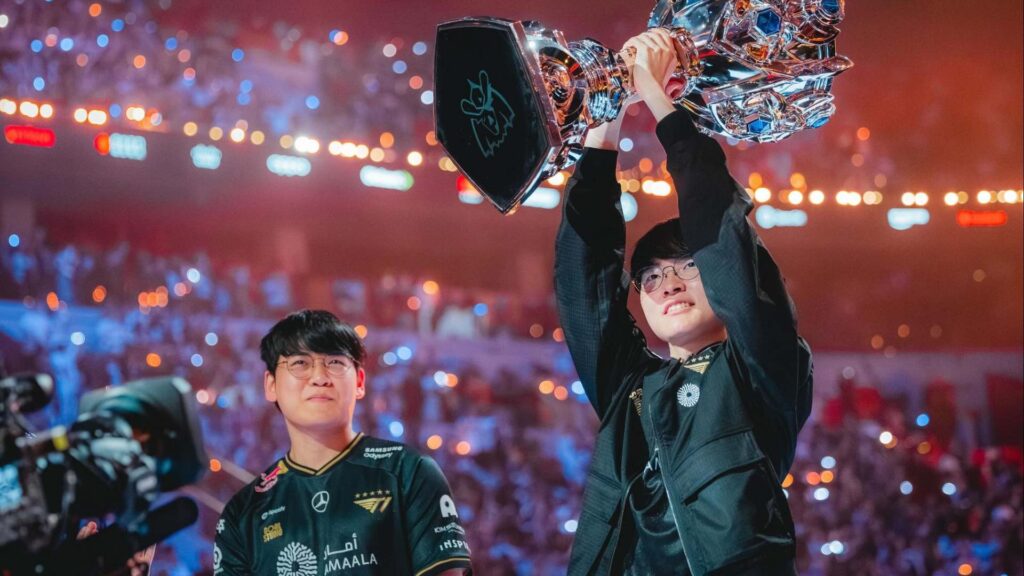 T1 players, including Faker and Gumayusi, celebrating Worlds victory with the Summoner’s Cup in front of a cheering arena.