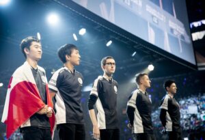 Five esports players in matching jerseys stand on stage under bright lights. One draped in a flag