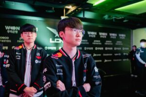 A focused young man in a gaming jacket stands with arms crossed, surrounded by team members in a dimly lit room with esports branding in the background