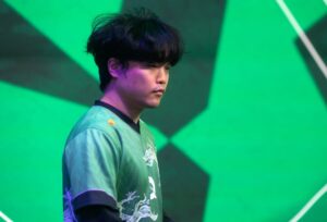 A person with dark hair stands focused against a bright green abstract background, wearing a green jersey with white patterns, conveying determination