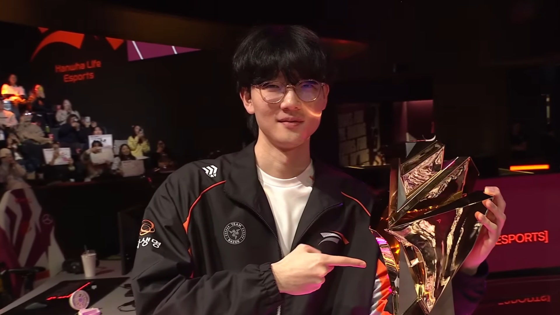 HLE Viper holding a gold trophy on stage and pointing at it with a smile