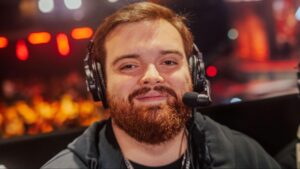 A League of Legends caster smiling while wearing a headset during a live broadcast