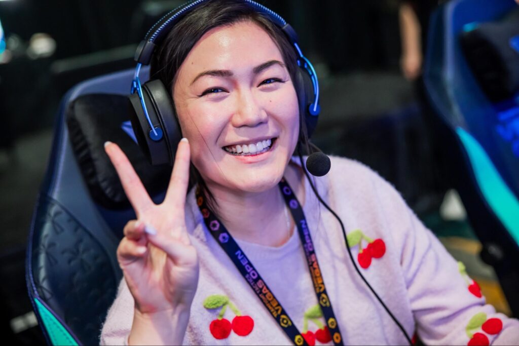 Rumay Hafu Wang wearing headset smiling and posing with peace sign during Hearthstone Battlegrounds event