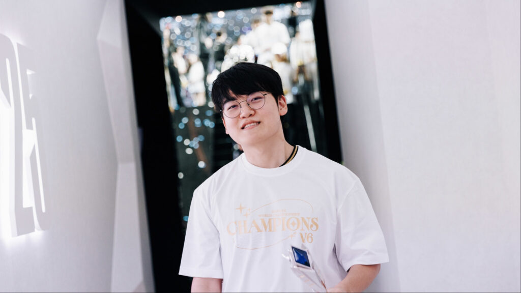 A man in a white championship shirt smiles indoors with blurred lights behind him