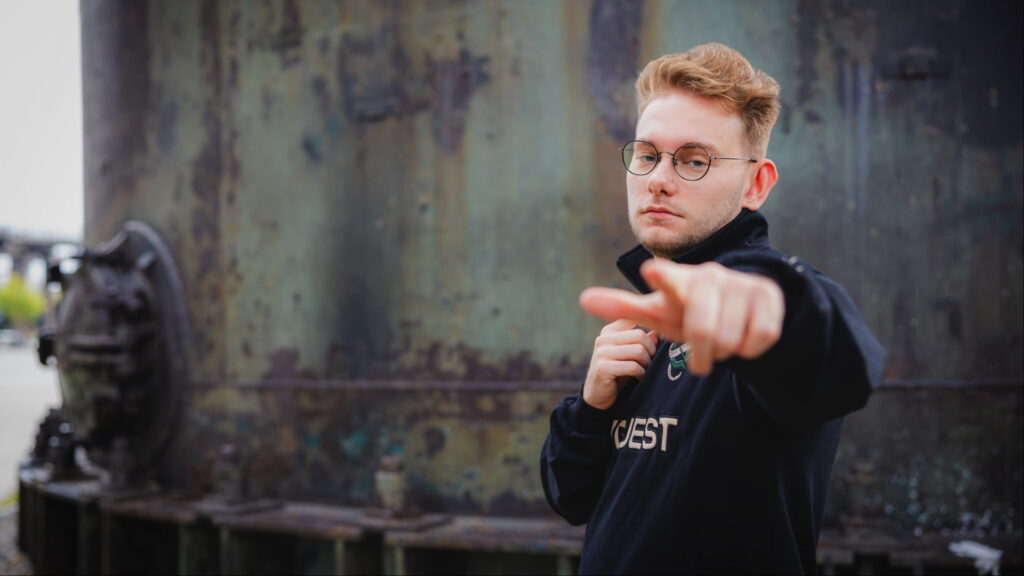A man in a black jacket points toward the camera outdoors