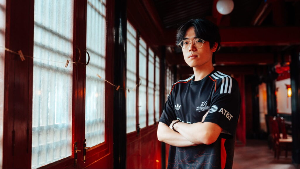 A man in an esports jersey stands with folded arms in a corridor with red wooden frames