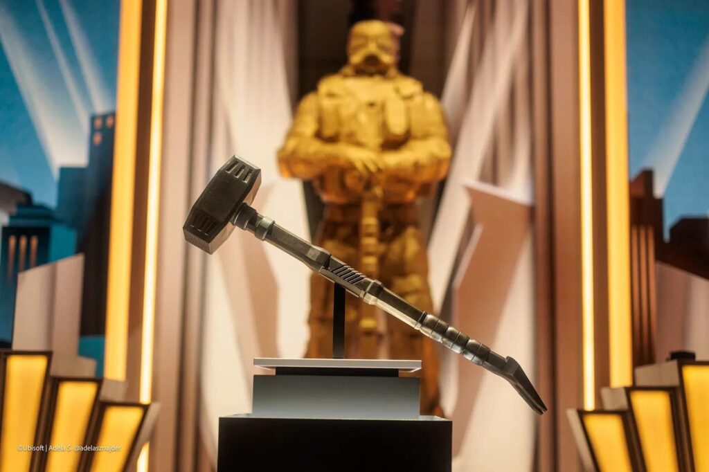 The image shows the Six Invitational 2026 hammer trophy displayed on a pedestal with a golden soldier statue blurred in the background