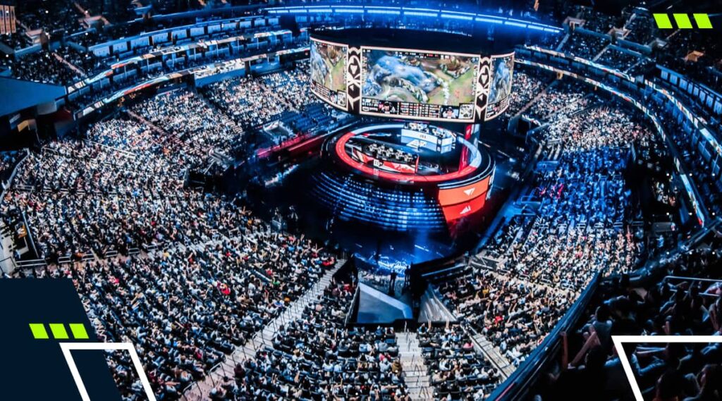 A massive crowd fills an arena for a League of Legends esports championship, watching the match on a giant central screen above the stage surrounded by lights and team booths.