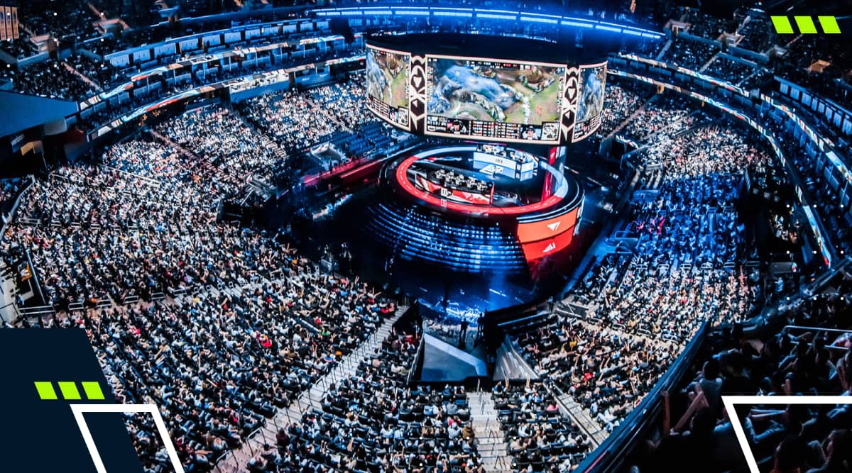 A massive crowd fills an arena for a League of Legends esports championship, watching the match on a giant central screen above the stage surrounded by lights and team booths.