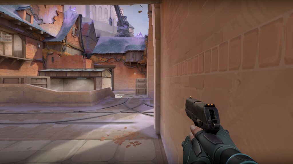 A VALORANT agent waits at a narrow corner with a pistol ready. The quiet market area ahead is covered in soft frost and scattered leaves