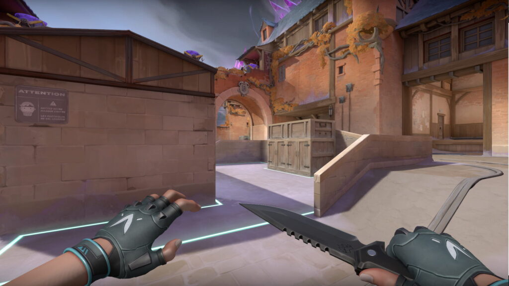 A VALORANT agent moves toward an archway marked by glowing lines. Wooden crates and warm brick walls frame the quiet entry point.
