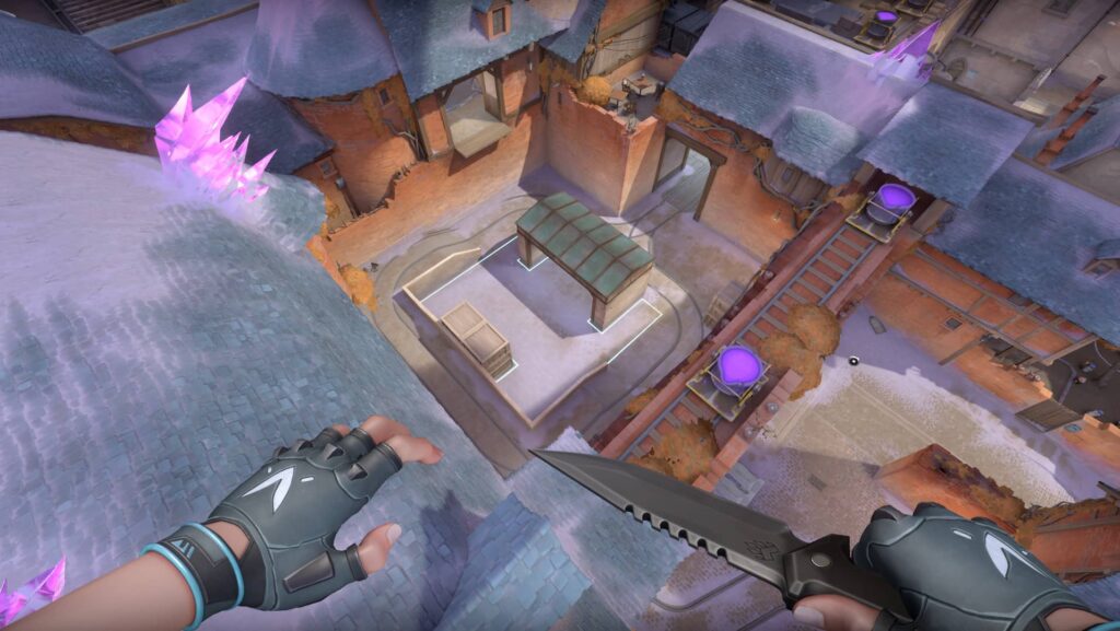 A VALORANT agent looks down at frozen rooftops glowing with purple crystals. The scene captures a high drop over a quiet street with a knife ready in hand