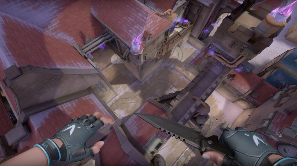 A VALORANT agent looks down from a snowy rooftop at a marked site with crates and a metal shelter. Purple crystals glow along the edges of the buildings