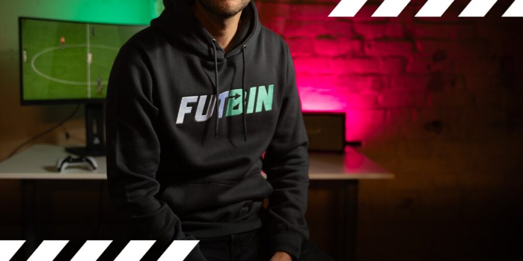Man wearing futbin hoodie with EA FC 26 gameplay in background