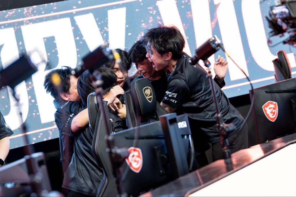 A League of Legends team celebrates emotionally around their gaming setup after winning a match
