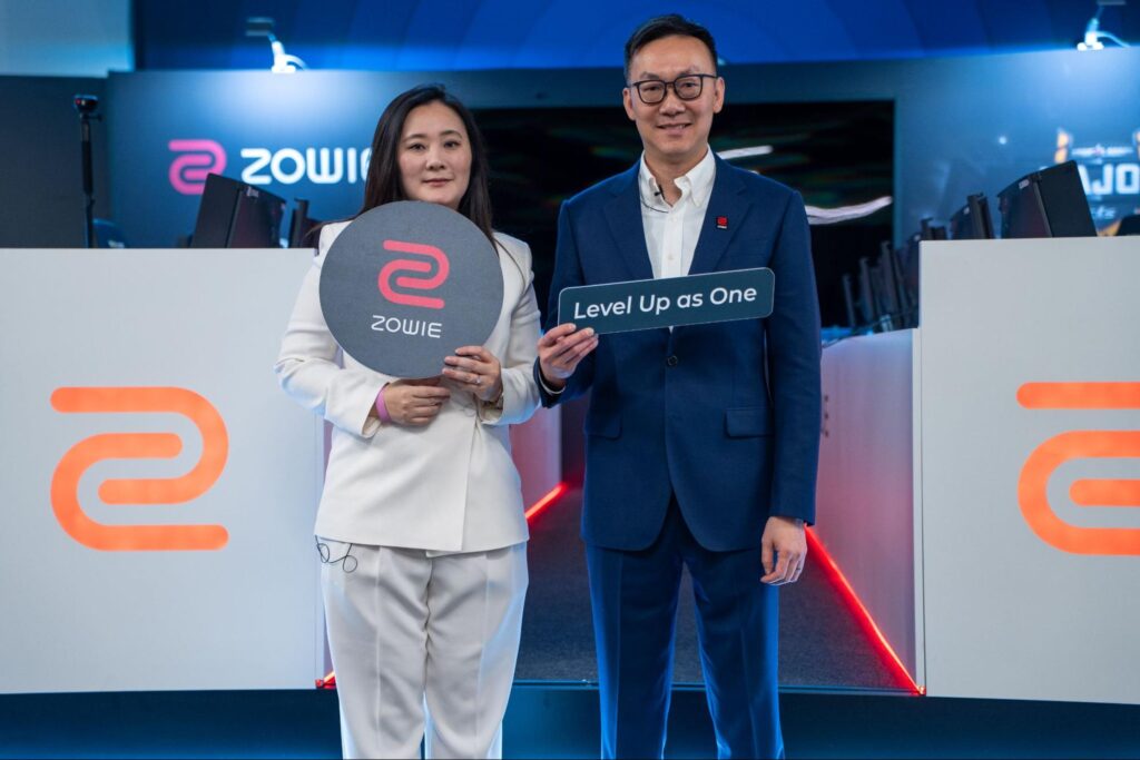 Two ZOWIE representatives standing on stage at a branded esports setup, holding ZOWIE signage during a media tour event, highlighting the company’s performance-driven esports philosophy