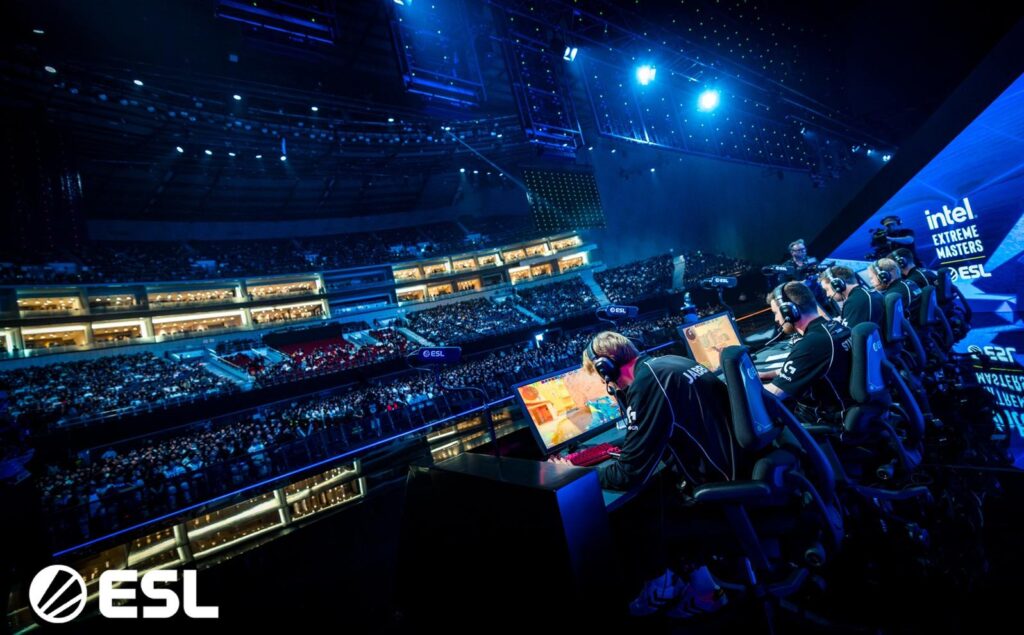Professional CS2 players competing on stage at an ESL Intel Extreme Masters event, playing Counter-Strike 2 in front of a sold-out arena.