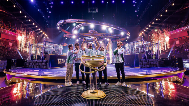 A Dota 2 team lifting a championship trophy on stage after winning a major esports tournament