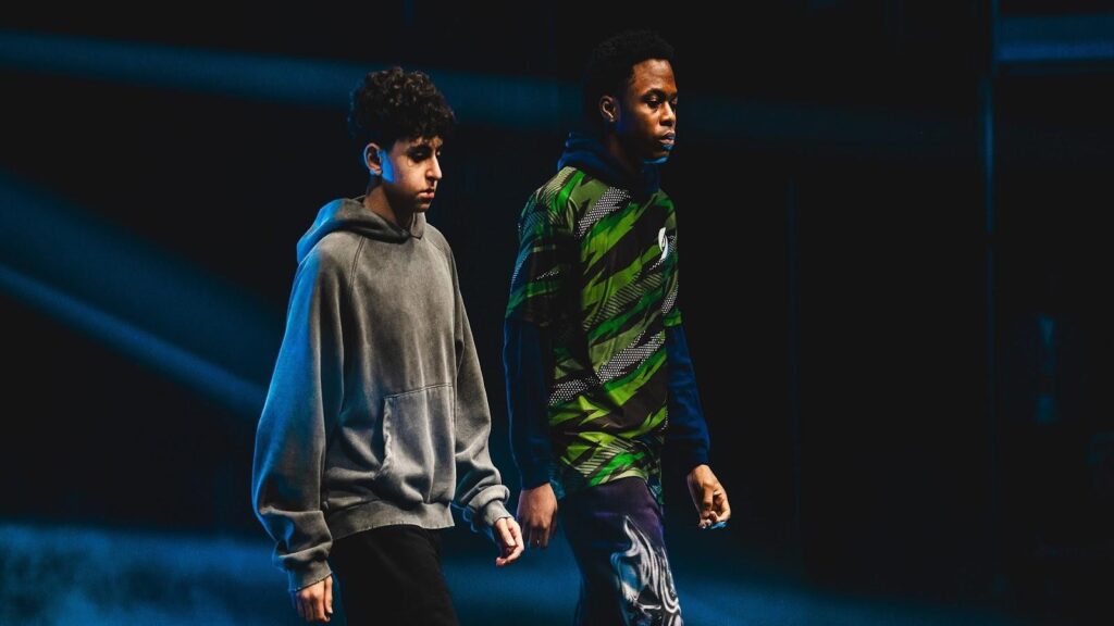 Two Fortnite esports players walking side by side on a dimly lit stage