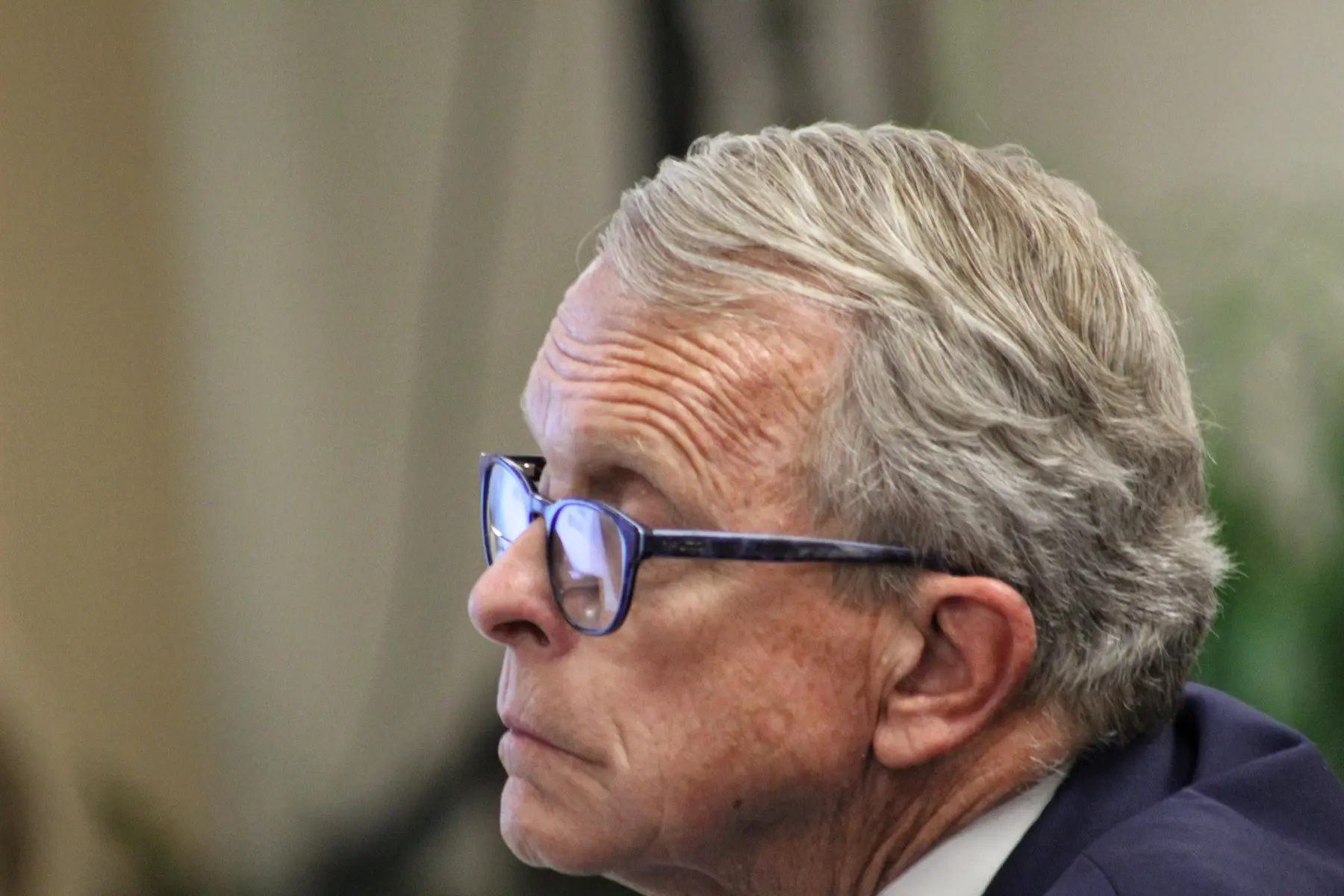 Close-up profile of Ohio Governor Mike DeWine wearing blue-rimmed glasses.